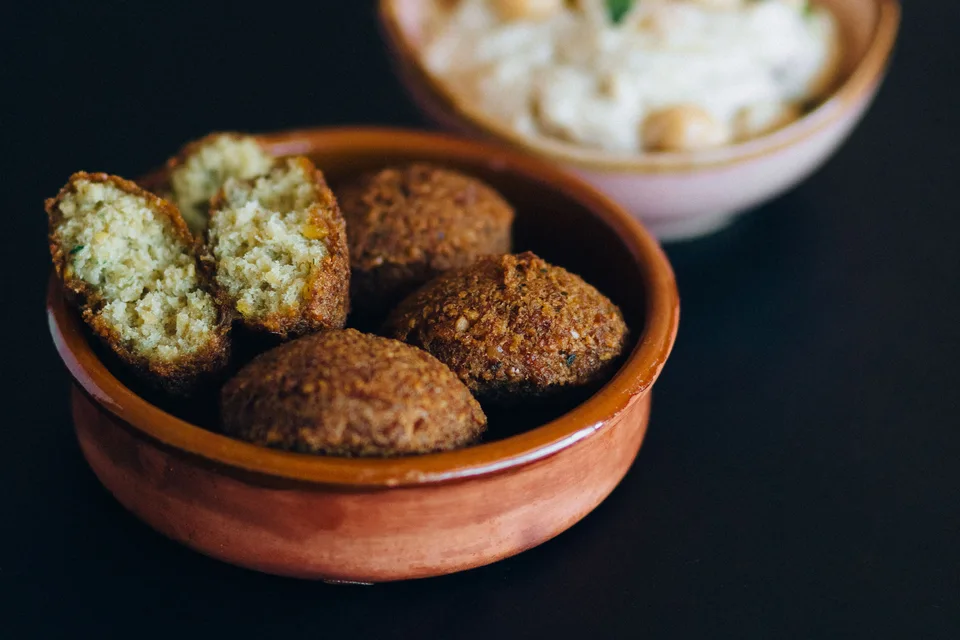 BookNoFees: Esimerkkikuva: Falafel-palloja, mukaan lukien yksi halkaistu pala, kulhossa, jonka takana on hummusta