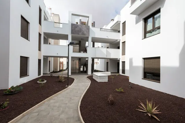 BookNoFees: semesterboende i Caleta De Fuste, Fuerteventura, Spanien – En innergård med stenlagd gångväg, vita byggnader och små växter i grusrabatter