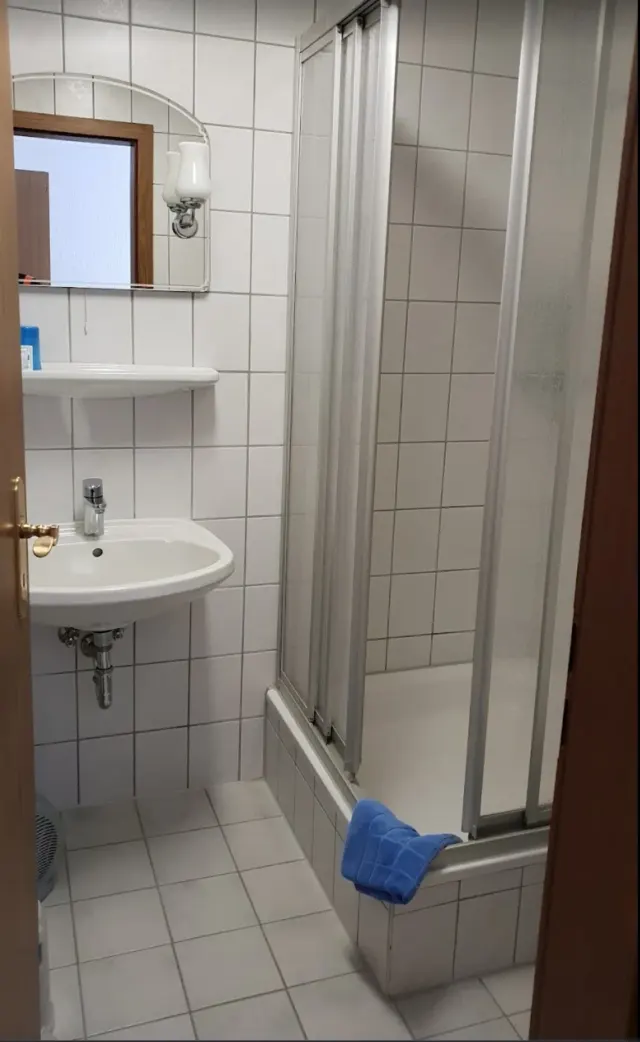 BookNoFees: semesterboende i Schönfeld, Sachsen, Tyskland – Badrum med vitt handfat, badkar med duschdörr och en blå handduk