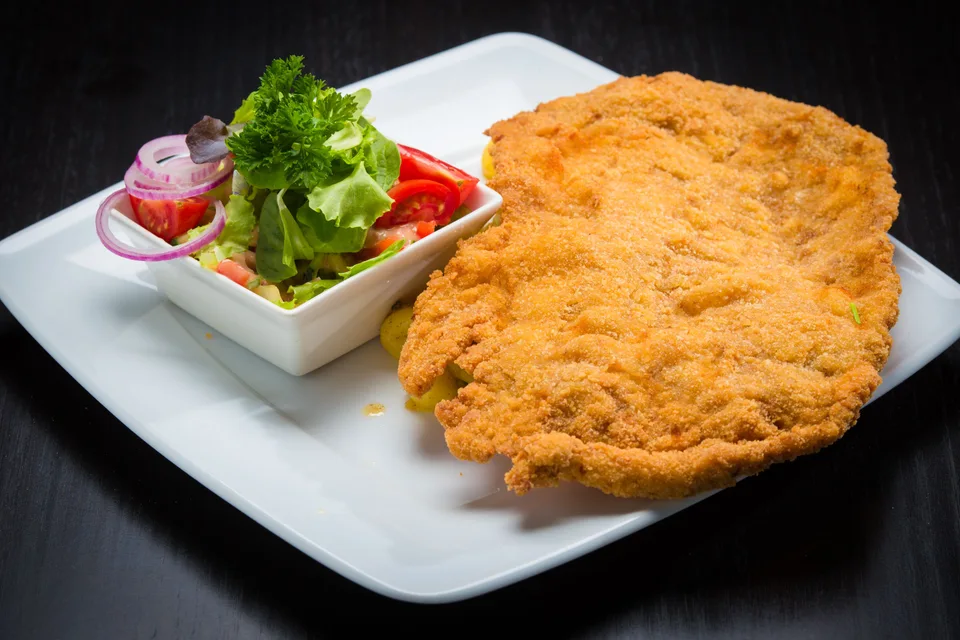 BookNoFees: Exempelbild: Panerad schnitzel med en sallad som tillbehör på en vit tallrik